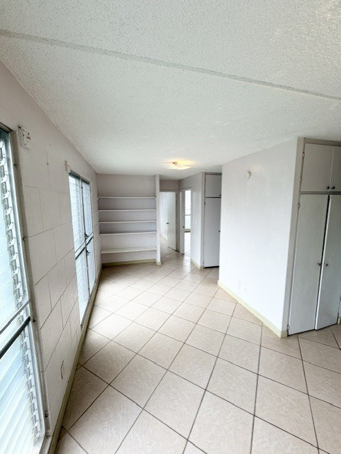 A white tiled kitchen and living room with a refrigerator, sink, and cabinets.